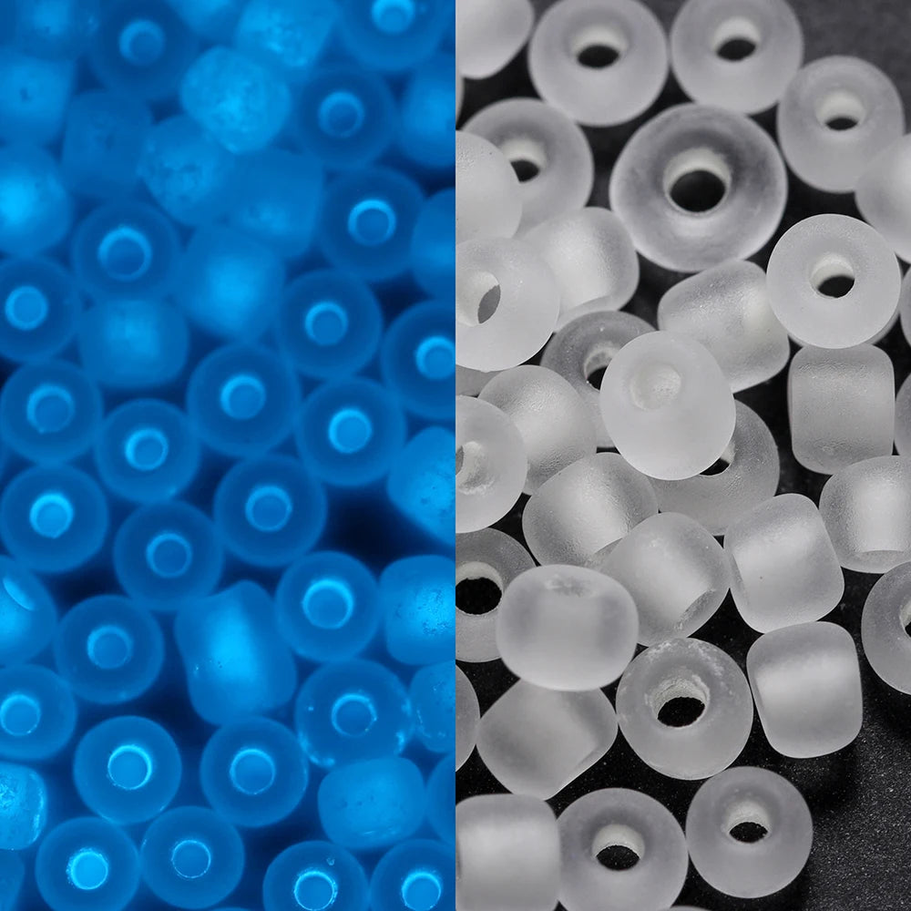 A close-up view of blue glow-in-the-dark glass seed beads and white plastic beads scattered on a dark surface.