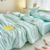 A light mint green summer seersucker quilt comforter spread across a bed with white bedding and a white stuffed animal.