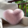 A fluffy pink heart-shaped fox fur throw pillow resting on a light-colored sofa.