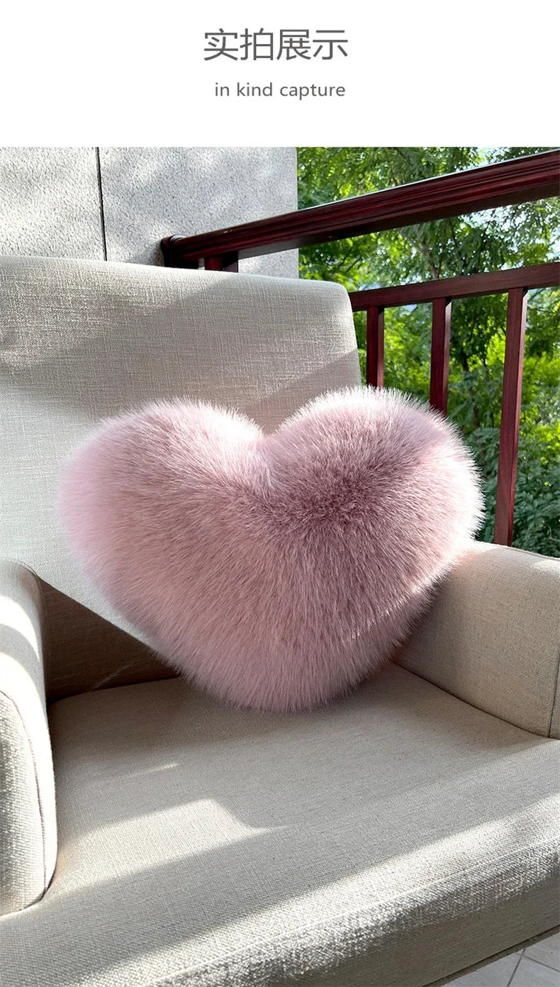 A fluffy pink heart-shaped fox fur throw pillow resting on a light-colored sofa.