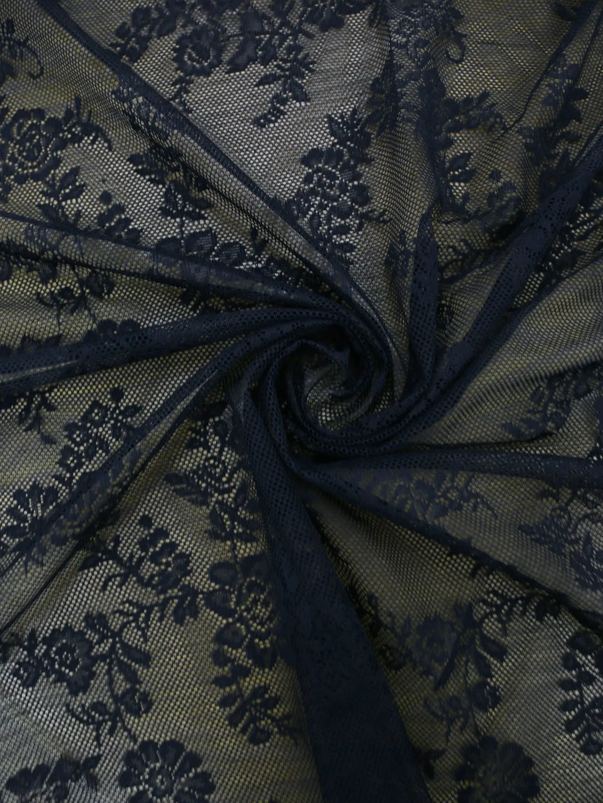 Dark blue floral lace sheer fabric gathered into a swirl, used as a curtain panel.