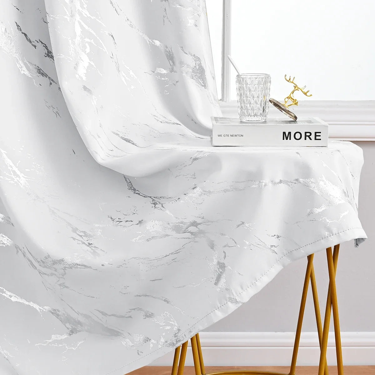 White curtain fabric featuring a marble print and silver stamping draped over a gold stand.