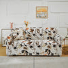 A beige stretch floral elastic sofa cover displayed on a light-colored wall with framed art.