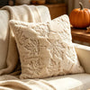 A cream fuzzy maple leaf throw pillow resting on a light-colored sofa with a beige throw blanket nearby.