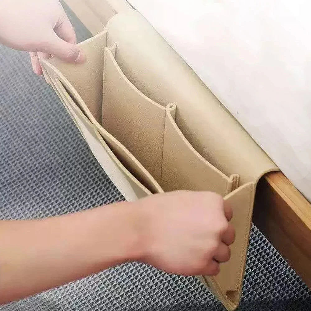 A hand is opening a felt bedside storage organizer with a hanging pocket, showing the interior structure.