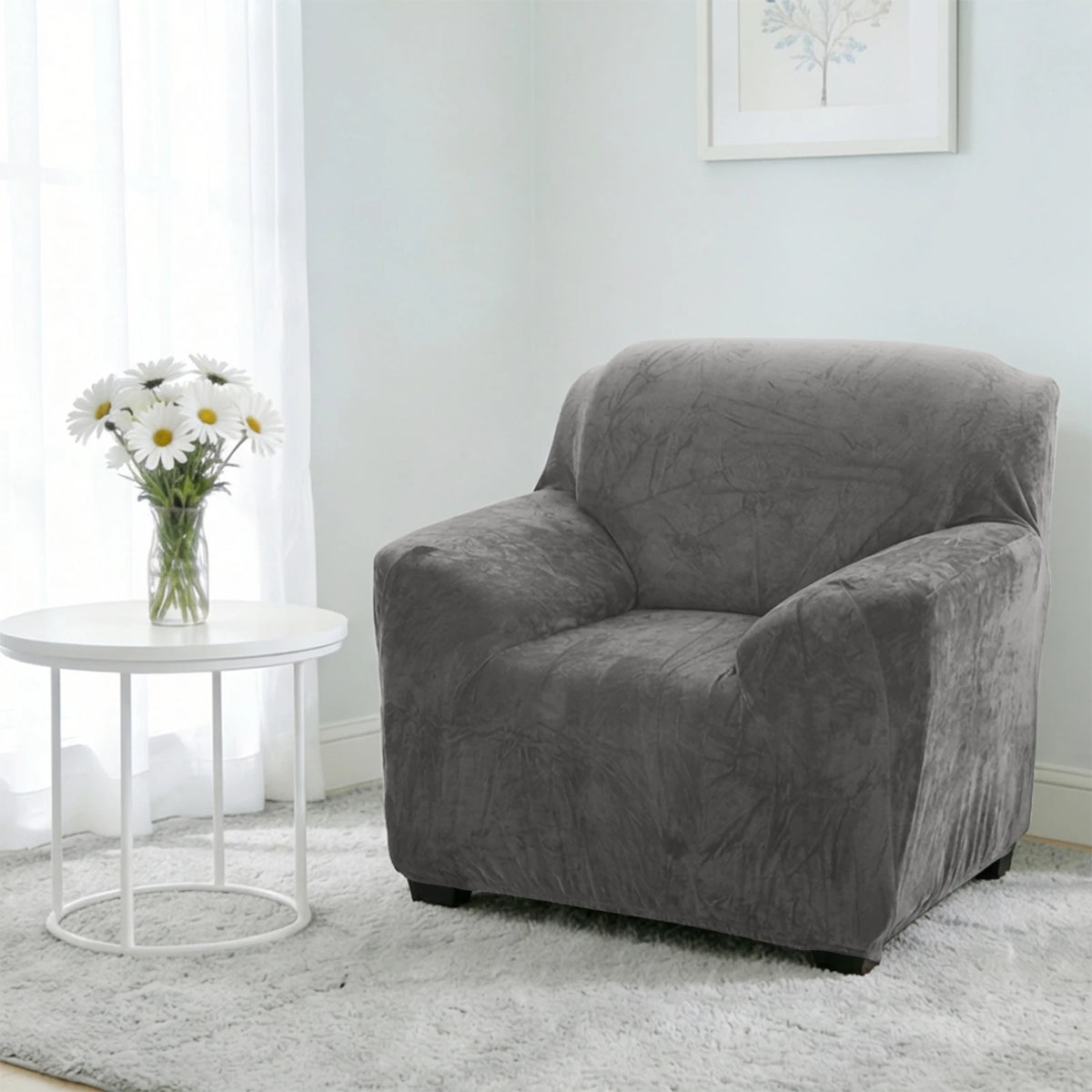 A gray stretch velvet sofa slipcover sits on a white round table in a bright room.