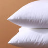 A close-up of two white breathable square core cushions resting on a light brown surface.