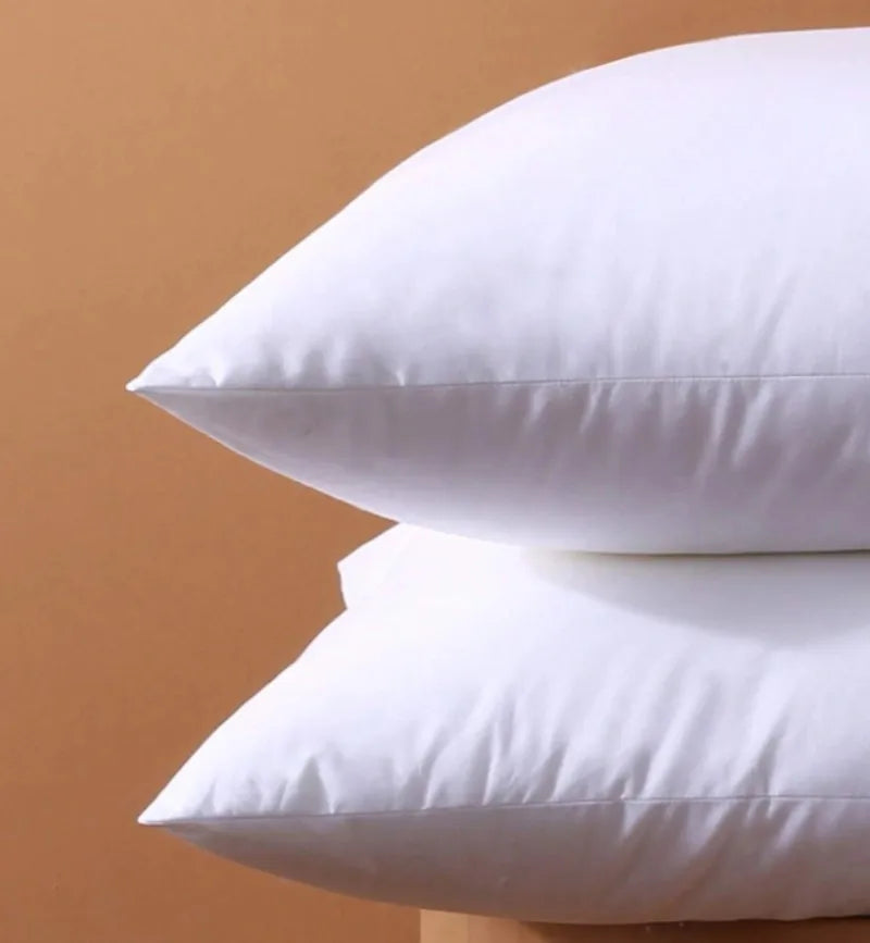 A close-up of two white breathable square core cushions resting on a light brown surface.