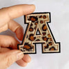 A leopard print iron-on alphabet patch letter A being held by a hand.