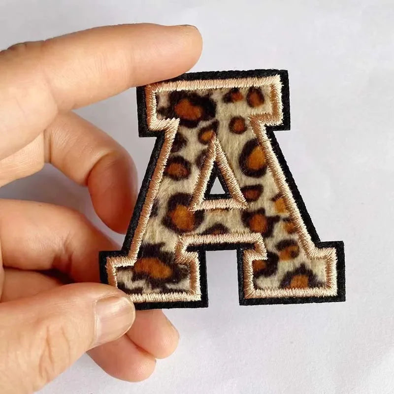 A leopard print iron-on alphabet patch letter A being held by a hand.