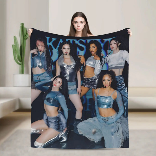 A woman holds up a black blanket featuring a K-Pop theme with various models and text.