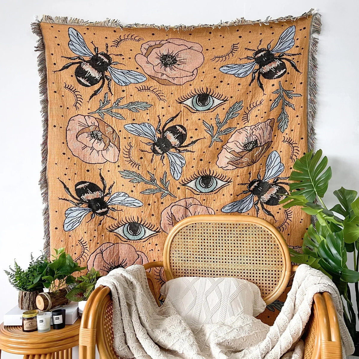 A bohemian geometric throw blanket featuring bees and eyes in earthy tones draped over a wooden chair.