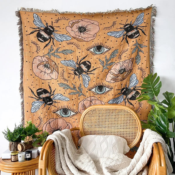 A bohemian geometric throw blanket featuring bees and eyes in earthy tones draped over a wooden chair.
