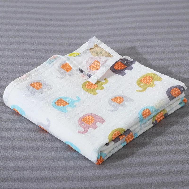 A folded white cotton muslin swaddle blanket featuring colorful elephant designs on a gray background.