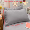A close-up of a matte gray pillowcase lying on a bed, with decorative string lights in the background.