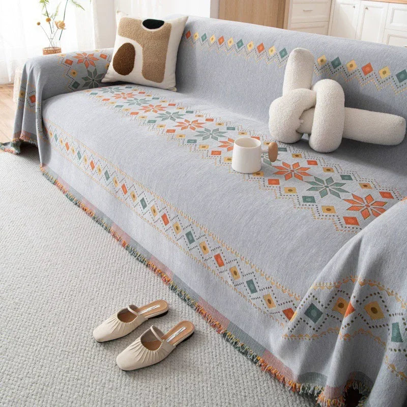 A light gray bohemian accent sofa cover featuring geometric patterns in orange, green, and white embroidery.
