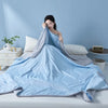 A light blue quilted quilt is spread out on a bed, with a woman resting her head on the fabric.