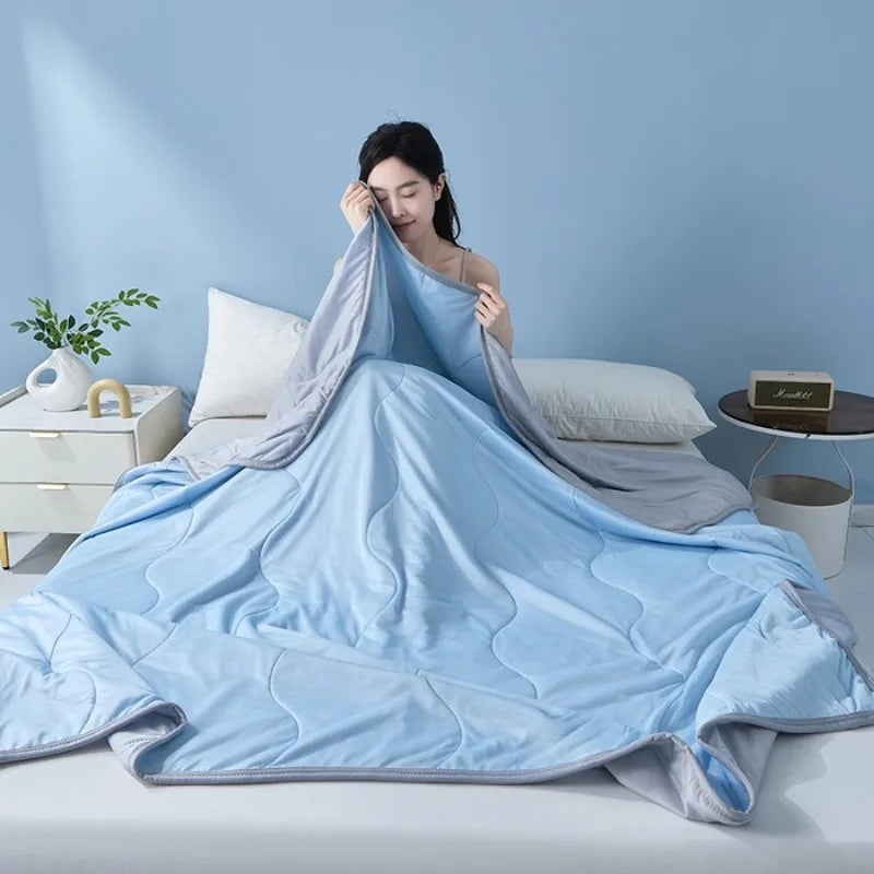 A light blue quilted quilt is spread out on a bed, with a woman resting her head on the fabric.