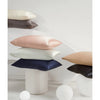 A stack of silk satin pillowcases in shades of pink, beige, and dark blue resting on a white surface.