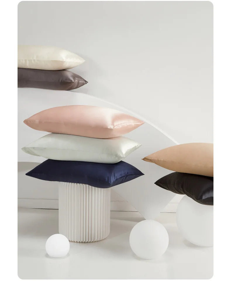 A stack of silk satin pillowcases in shades of pink, beige, and dark blue resting on a white surface.