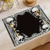 A black placemat featuring a vintage skull and floral design with gold cutlery.
