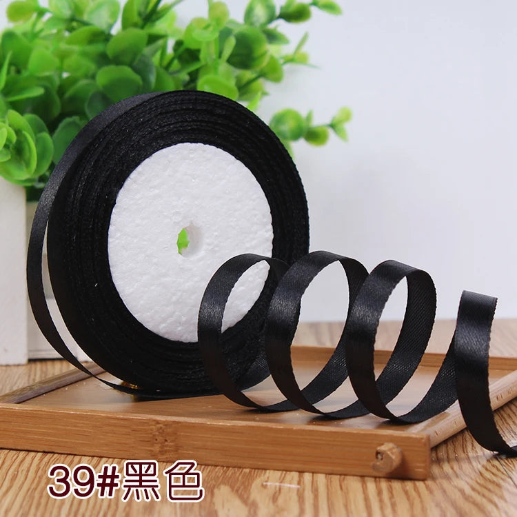 Rolls of black satin ribbon with white filling visible on a wooden surface