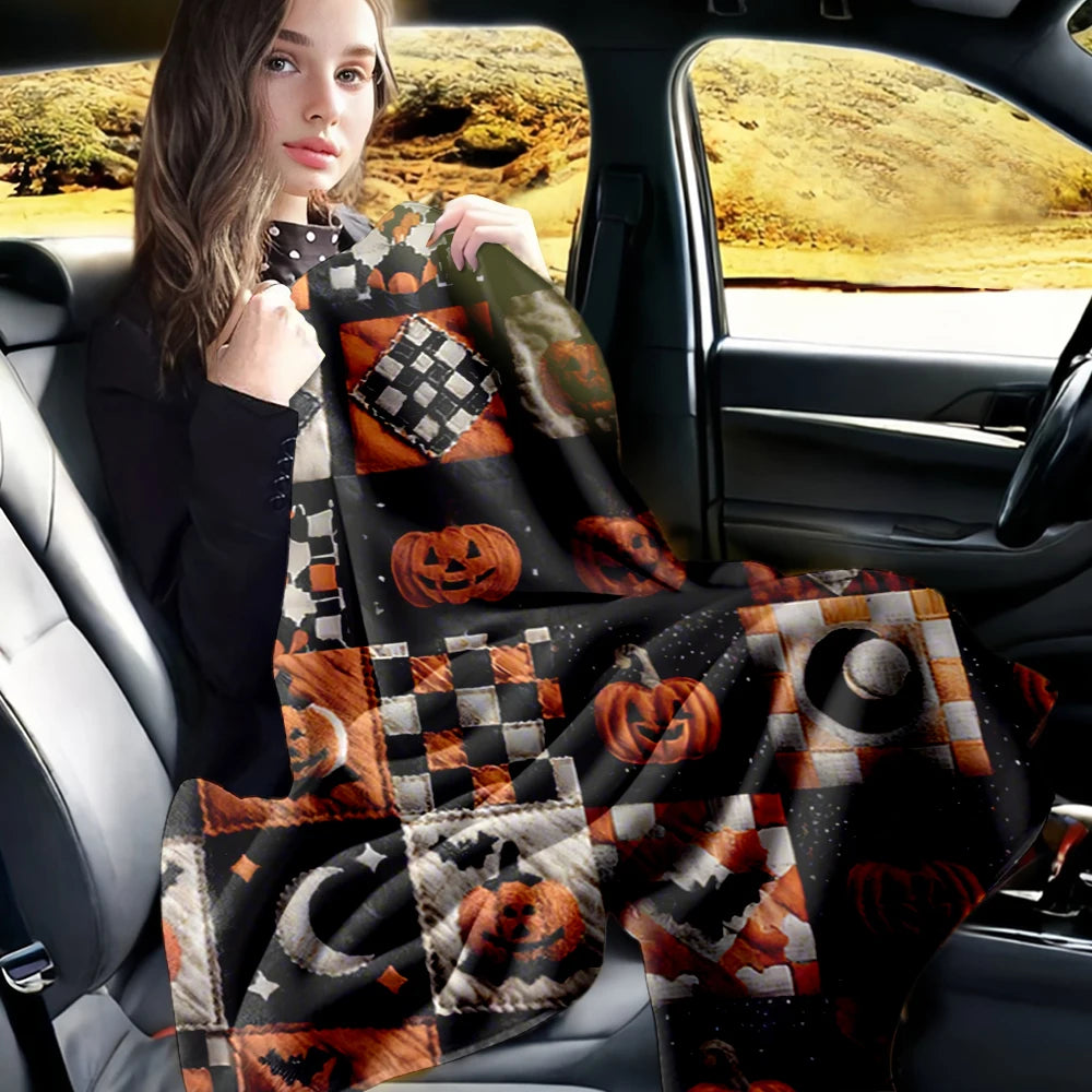 A woman sits in a car, holding and displaying a black and orange patchwork flannel throw blanket with Halloween designs.