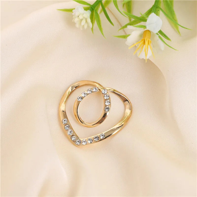 Gold-toned metal ring clips with clear stones resting on a soft beige fabric next to white flowers.