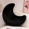 A black moon-shaped throw pillow resting on a white surface.