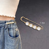 A gold-toned adjustable pearl brooch with seven white pearls is shown against a denim background.