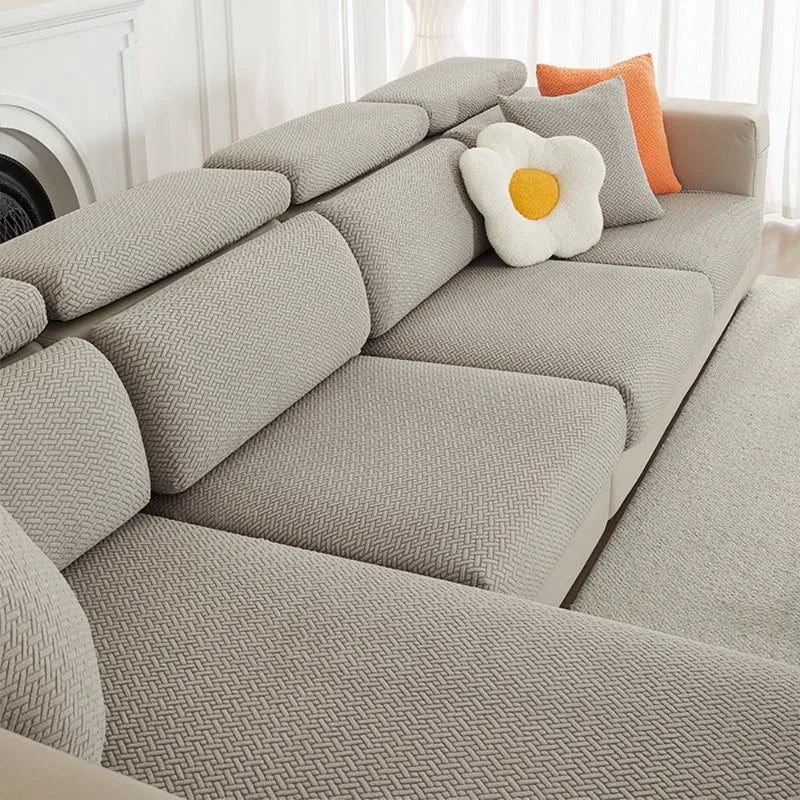 A light gray jacquard elastic sofa cushion slipcover with an orange accent pillow on a modern sofa.