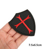 Black embroidered military cross shield hook and loop patch shown on a hand.