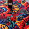 A dark glass bottle sits on a vibrant red and orange bohemian printed linen fabric surface.
