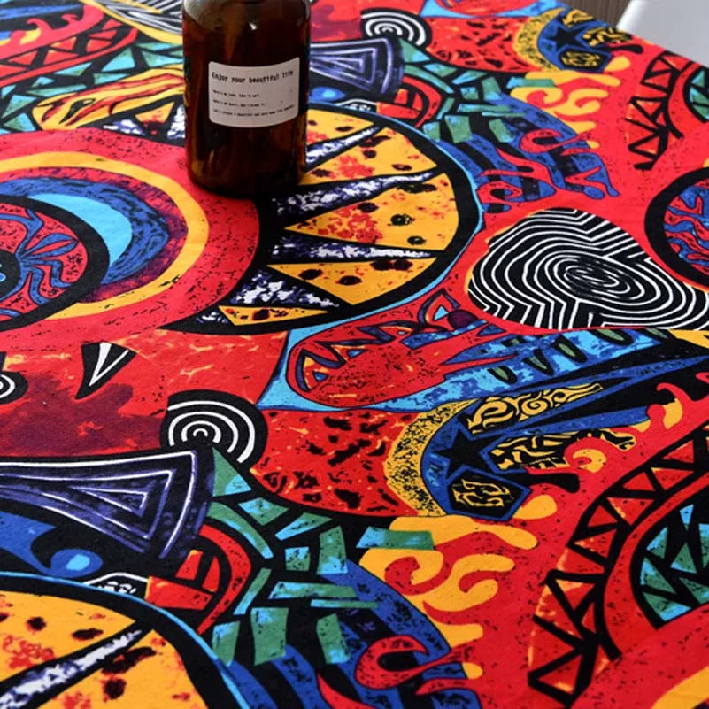 A dark glass bottle sits on a vibrant red and orange bohemian printed linen fabric surface.