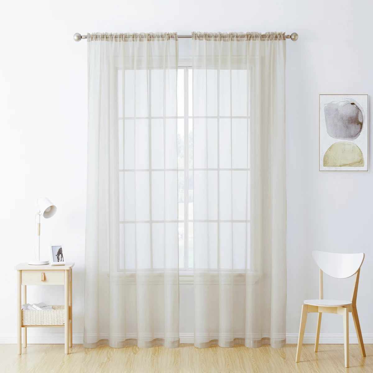 Sheer white voile curtains hanging in a window with a wooden chair nearby.