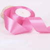 Pink satin craft ribbon rolled on a spool with a natural fiber material nearby.