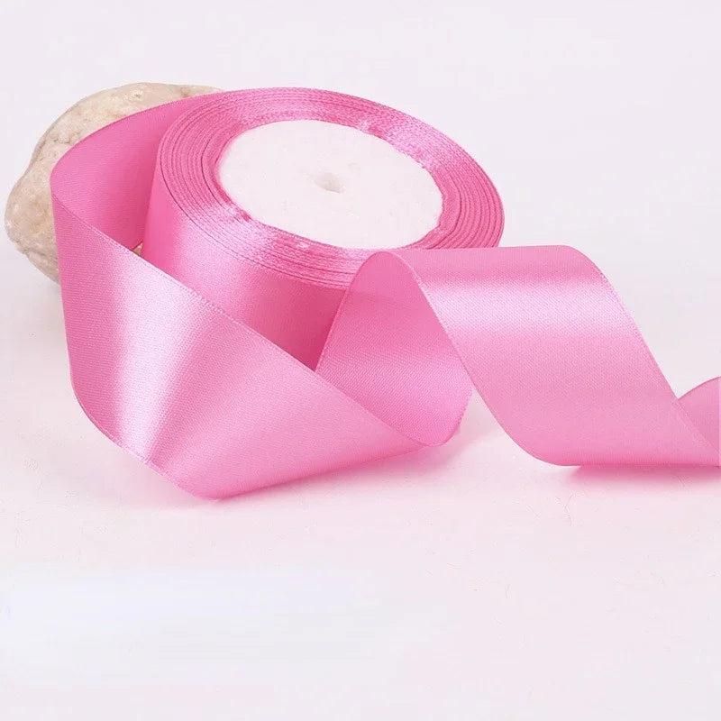 Pink satin craft ribbon rolled on a spool with a natural fiber material nearby.