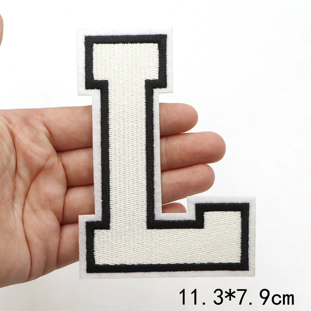 A hand holds a white embroidered letter I patch with black outline on a white background.