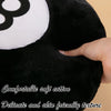 A close-up of a black plush toy with a white circle patch and a hand touching the fabric.