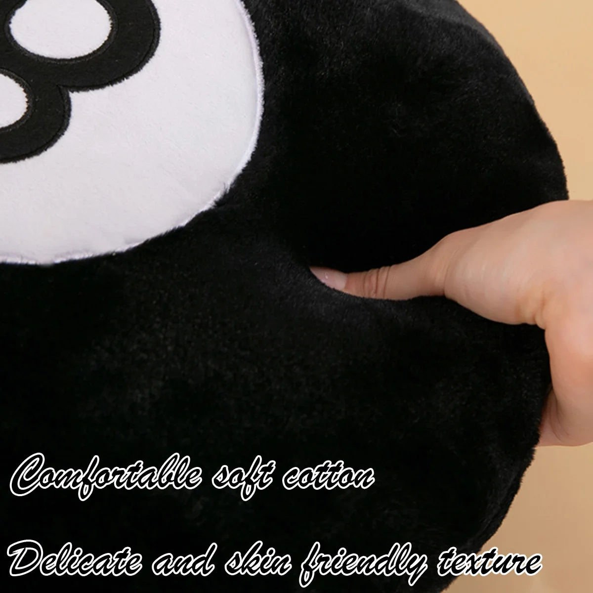 A close-up of a black plush toy with a white circle patch and a hand touching the fabric.