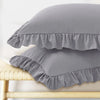A set of two gray pillow covers with ruffled envelope closures resting on a light wooden surface.