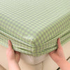 Hands are holding up a light green checkered fitted sheet to show its texture and fit.