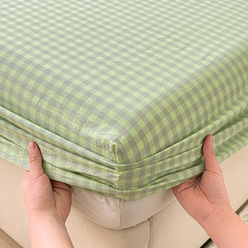 Hands are holding up a light green checkered fitted sheet to show its texture and fit.