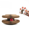 A hand holds a white cat paw-shaped object, next to a brown, textured scratching board with a red, spotted item inside.