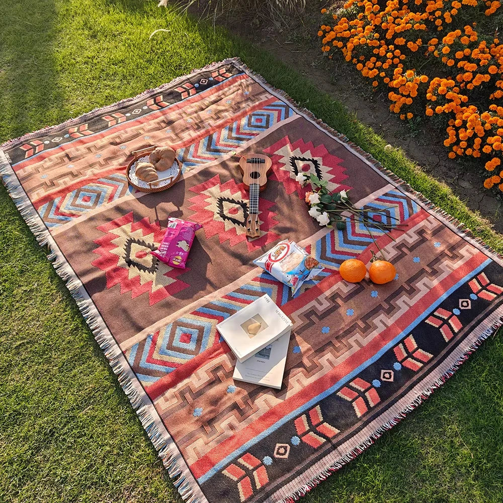 A patterned knit blanket with geometric designs in earth tones laid out on green grass.