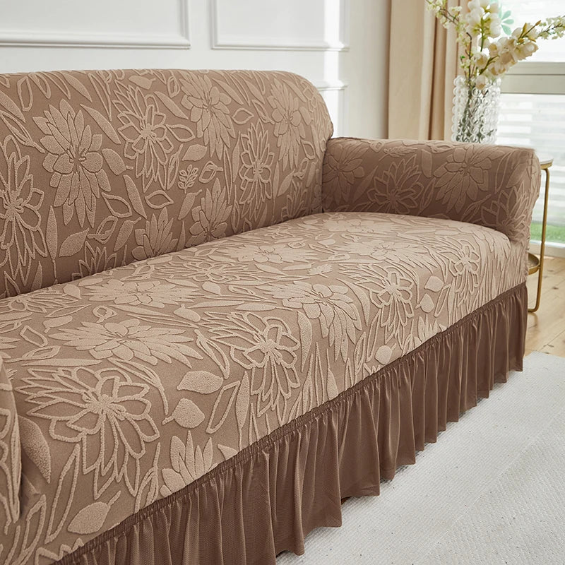 A tan jacquard stretch sofa cover featuring a floral pattern and a ruffled hem.