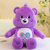 A purple Care Bears Rainbow Bear plush toy with pink heart accents sitting on a white surface.