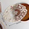 Elegant oval lace embroidered coaster featuring floral details and a crown motif on a wooden surface.