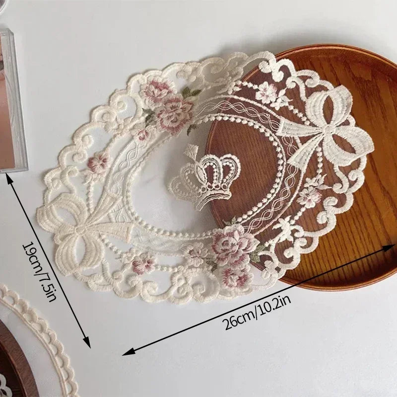 Elegant oval lace embroidered coaster featuring floral details and a crown motif on a wooden surface.