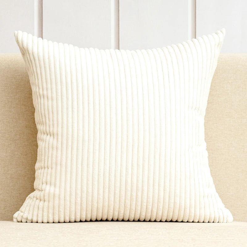 A cream-colored, vertically ribbed throw pillow cover resting on a light-colored sofa.